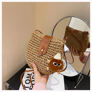 Macro shot of straw crossbody bag with brown leather flap and cute plush monster charm