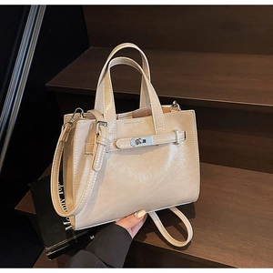 Detail of beige square handbag with silver buckle closure on a wooden staircase