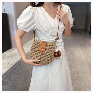 Detail of woven straw crossbody bag with brown leather flap and cute plush doll pendant