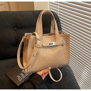 Detail view of beige PU leather handbag with silver lock on a soft velvet sofa