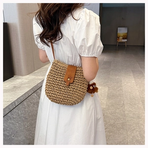 Detail of woven straw bag with brown leather flap and cute animal charm on strap