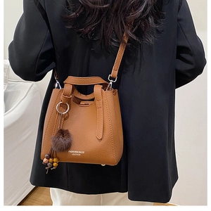Sac seau en cuir marron avec breloque en bois porté par un mannequin en blazer noir