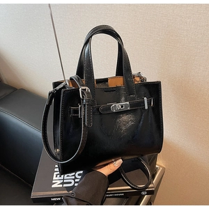 Detail of a black glossy leather handbag with a metal buckle and adjustable shoulder strap
