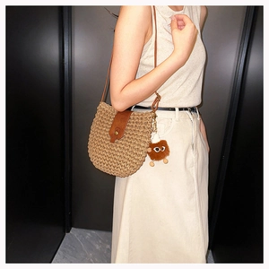 Detail of woven straw shoulder bag with leather flap and cute plush monster charm