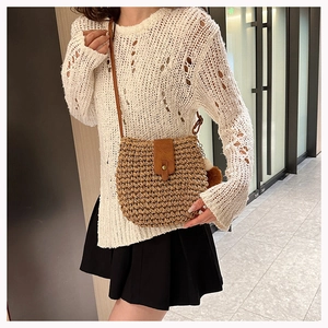 Detail of hand-woven straw crossbody bag with brown leather strap and pom-pom charm