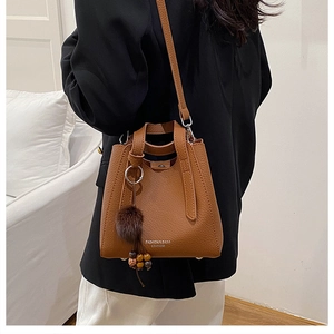 Sac seau en cuir marron grainé avec breloque en peluche porté par un mannequin