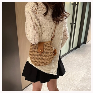 Detail of hand-woven straw crossbody bag with leather strap and decorative pompom charm