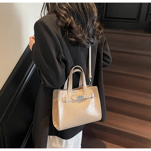 Detail of a beige leather handbag with silver turn-lock clasp shown in a lifestyle setting