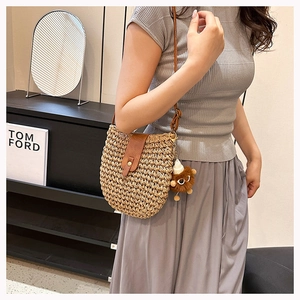 Detail of hand-woven straw crossbody bag with brown leather strap and monster charm