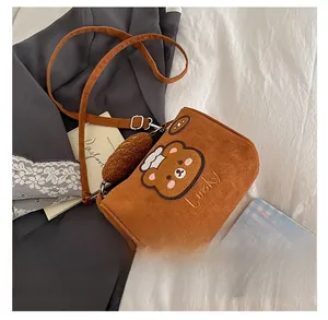 Detail view of brown suede crossbody bag with teddy bear embroidery and pompom charm