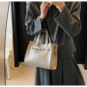 Detailed view of champagne tote bag with metal lock buckle on gray blazer outfit