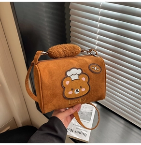 Detail of brown cylinder crossbody bag featuring teddy bear embroidery and fuzzy handle