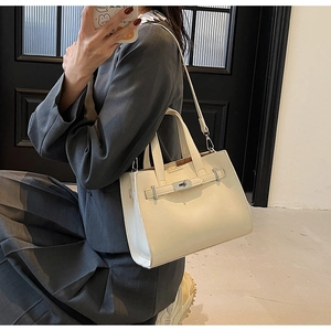 Close-up of cream structured PU leather tote with metal clasp on a gray blazer model