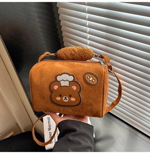 Detail of a brown suede cylinder bag featuring a chef bear patch and Lucky embroidery