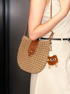Woven straw crossbody bag with brown leather flap and bear charm shown on model