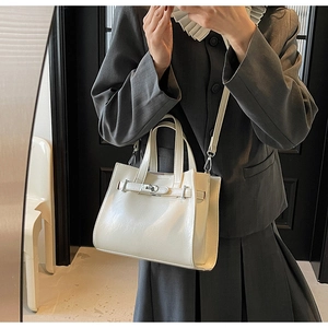 Detail of cream leather tote bag with silver buckle and thin strap shown on a model