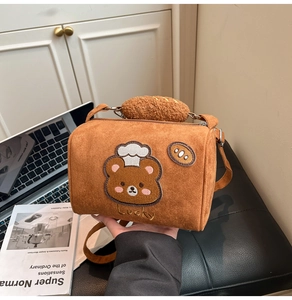 Detail of a brown cylinder bag featuring a cute chef bear embroidery and Lucky text