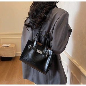 Detail of a black glossy leather tote bag showing the silver metal buckle and handle texture