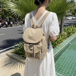 Beige lightweight nylon backpack featuring top flap buckle closure and front storage pocket