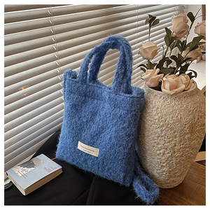 Detail of dark blue plush wool handbag showing soft texture and woven label in soft light