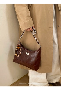 Detail of dark red quilted chain bag featuring a silver metal twist lock and bead charm
