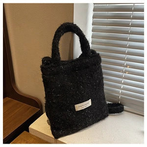 Detail of black tweed tote bag featuring silver glitter threads and a woven brand label