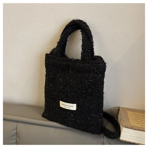 Detail of black wool texture handbag featuring original design label and soft material