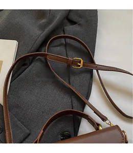 Detail of adjustable long shoulder strap with gold buckle on brown leather bag