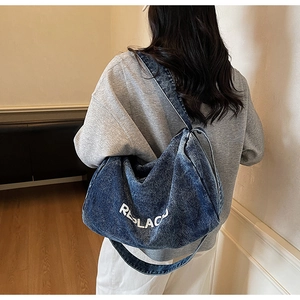 Model wearing a large navy blue washed denim hobo bag with white REPLACE printed text