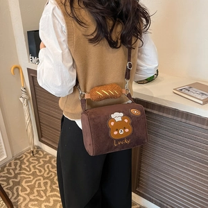 Detail of a plush bear crossbody bag featuring embroidered Lucky text and a bread strap