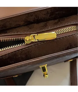 Close-up of golden metal zipper and hardware on coffee brown leather crossbody bag