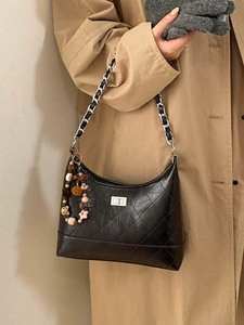 Quilted black chain shoulder bag with cute bead charm shown on a khaki trench coat