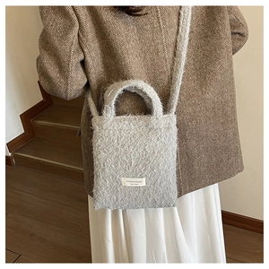 Close-up of light gray woolly crossbody bag with brand label and stylish knit texture