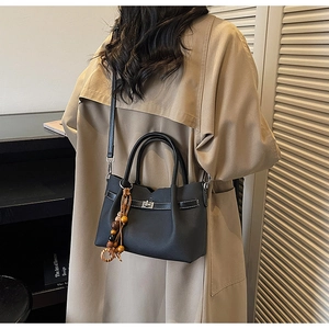 Détail d'un sac bandoulière en cuir noir avec breloque en bois sur un trench-coat kaki