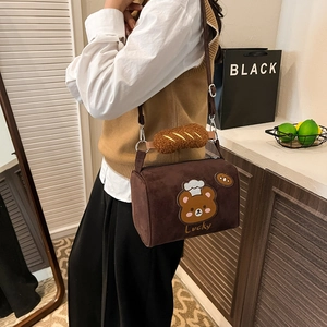 Close-up of brown suede pillow bag featuring a bear embroidery and a bread-shaped charm