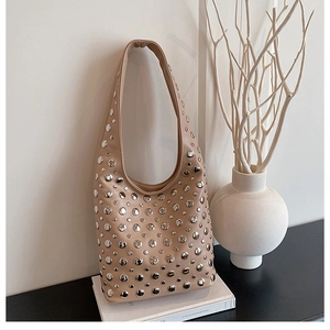 Detail of beige hobo shoulder bag featuring decorative silver rivets in a minimalist setting