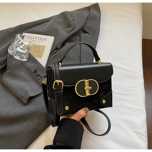 Detail of vintage black crossbody box bag with gold oval lock on white cloth