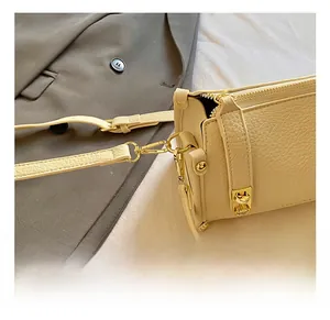 Close-up of golden metal hooks and textured lychee leather on a beige shoulder bag