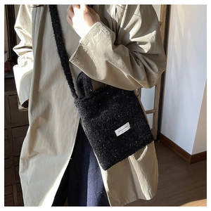 Close-up of black fuzzy wool crossbody bag with brand patch worn on beige trench coat