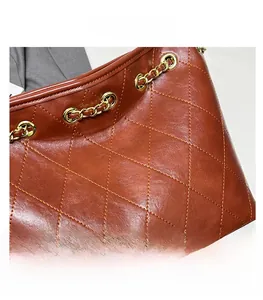 Close-up of brown quilted leather texture with gold chain link details on tote bag