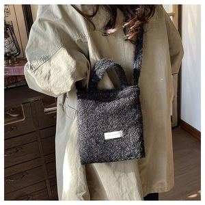 Detail of black wool tote bag showing texture, woven handles, and minimalist brand label
