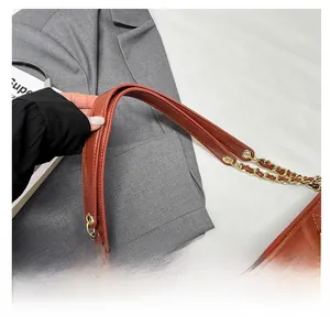 Detail of quilted brown leather tote bag with wide strap and gold chain accent