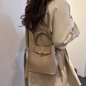 Detailed view of beige pebble leather bucket bag with gold lock and thin shoulder strap