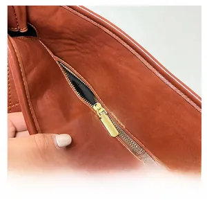 Detail of a smooth gold metal zipper on a dark red-brown quilted leather tote bag