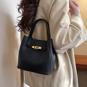 Black lychee leather bucket bag with gold buckle shown on model in light suit