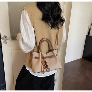 Détail du sac à main en cuir beige avec poignées brunes et breloque à pompon en perles
