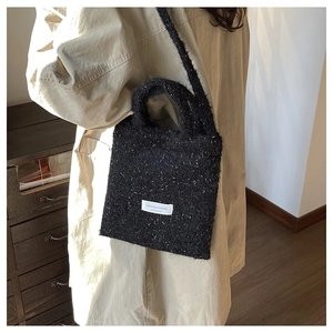 Detail of black woolly bucket bag with shimmering silver accents and branded fabric label