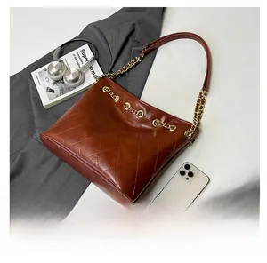 Detail of dark brown quilted leather tote bag with gold chain strap on soft fabrics