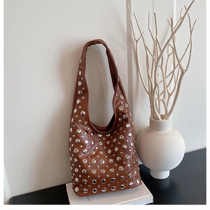 Detail of a brown leather hobo bag with large silver studs on a white book stand