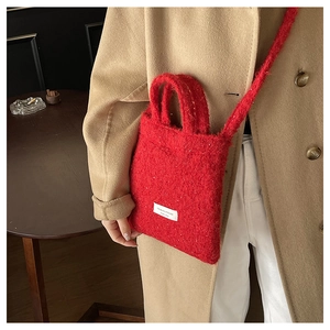 Detail of red fuzzy wool tote bag with white woven label on camel winter coat